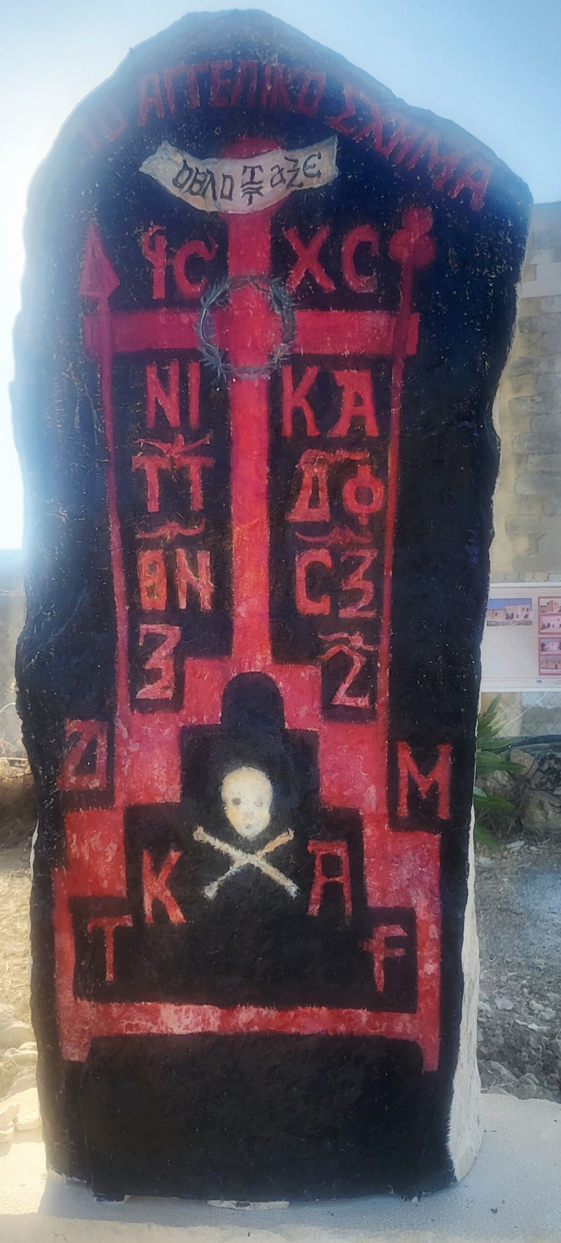 Painted stone monument at St. George’s Monastery – red Byzantine cross, Greek inscriptions, skull and crossbones.